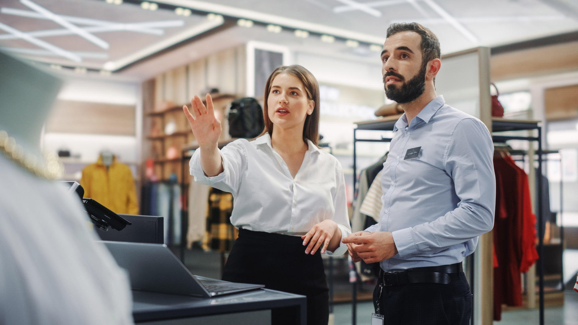 Clothing Store: Businesswoman Uses Laptop Computer, Talks to Visual Merchandising Specialist, Collaborate To Create Stylish Collection.